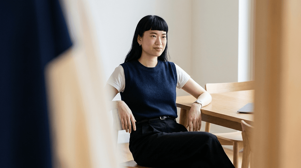 Woman in a navy sweater vest seated beside a wooden desk