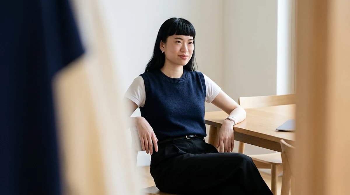 Woman in a navy sweater vest seated beside a wooden desk