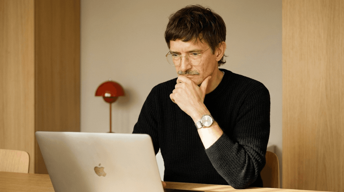 Man with glasses considering his work on a laptop