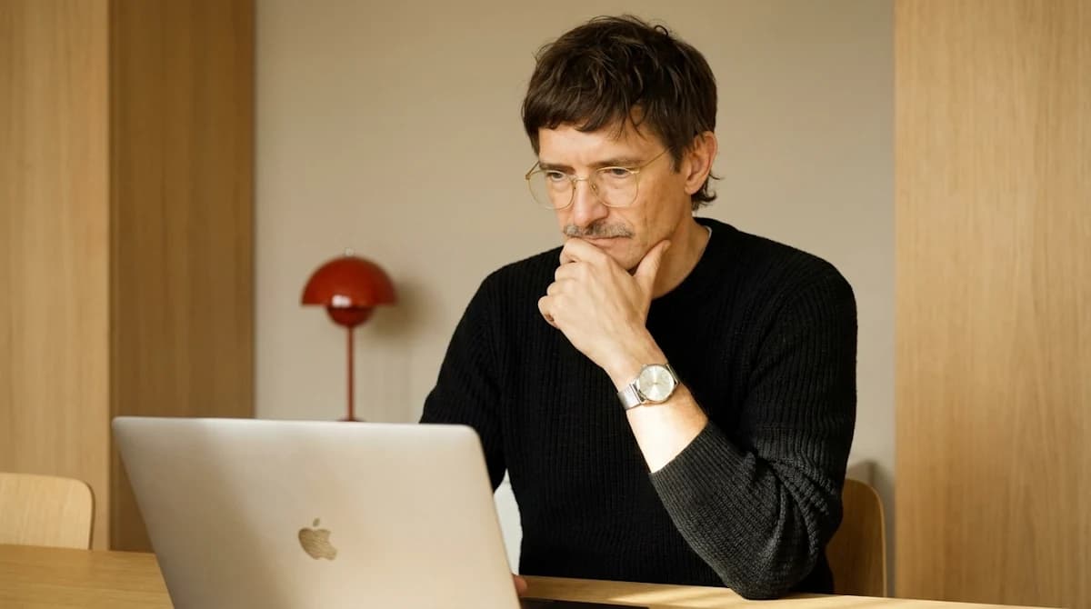 Man with glasses considering his work on a laptop