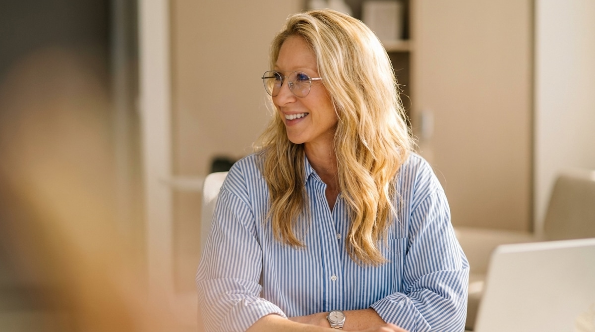 A woman with glasses in a blue striped shirt seated at a table