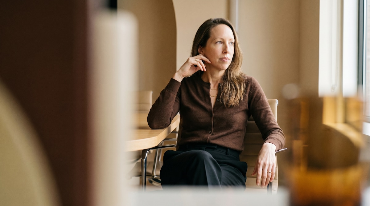 A woman in a brown cardigan seated beside a bright window